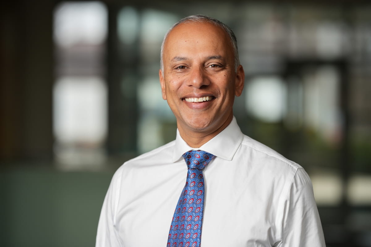Headshot of Chandy John in white button up and tie smiling at camera 