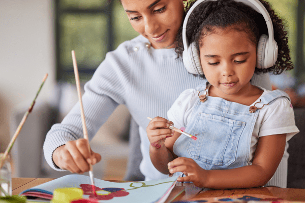 Autistic child wearing headphones while painting with mother. 