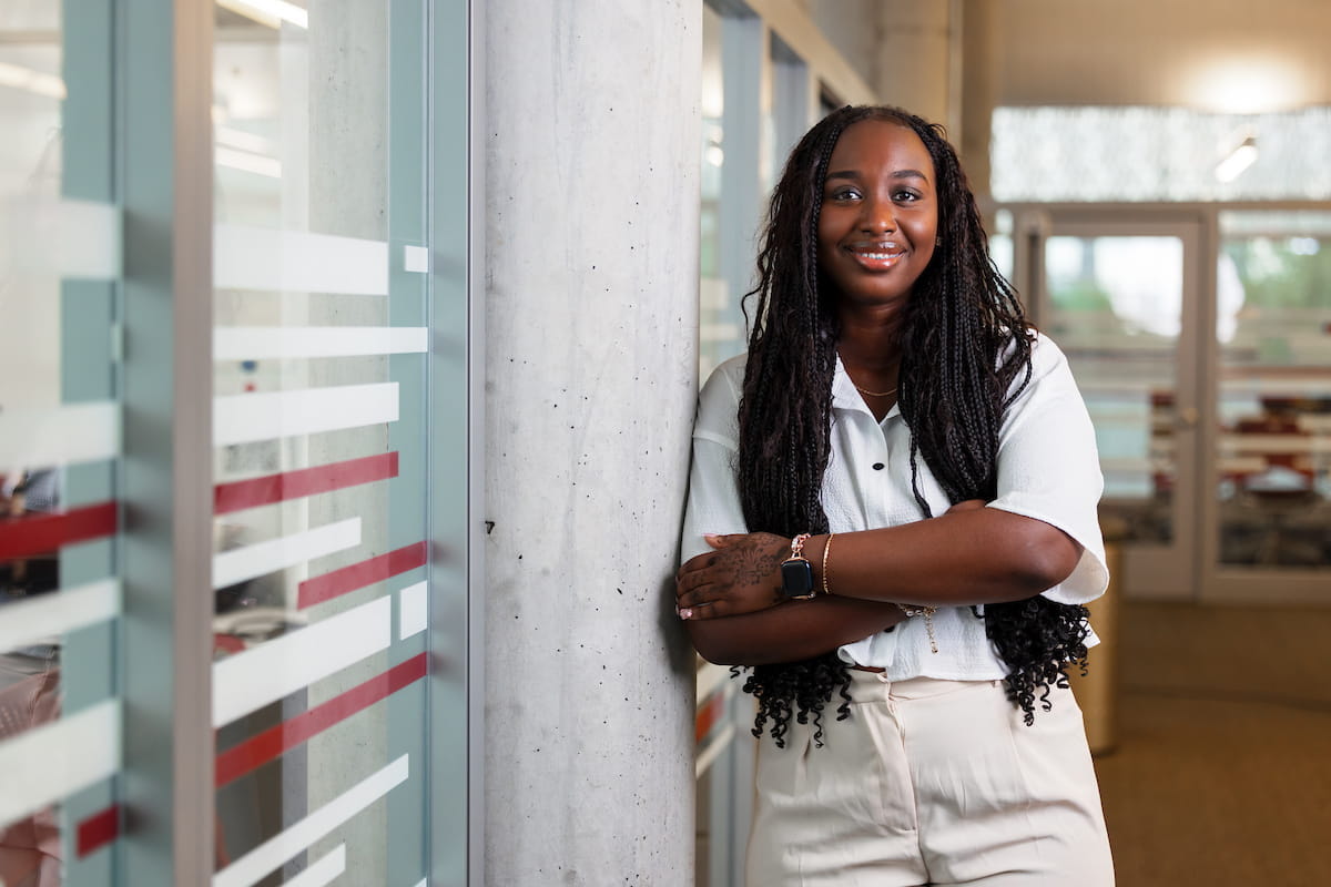 A young black woman smiles at the camera with her arms crossed