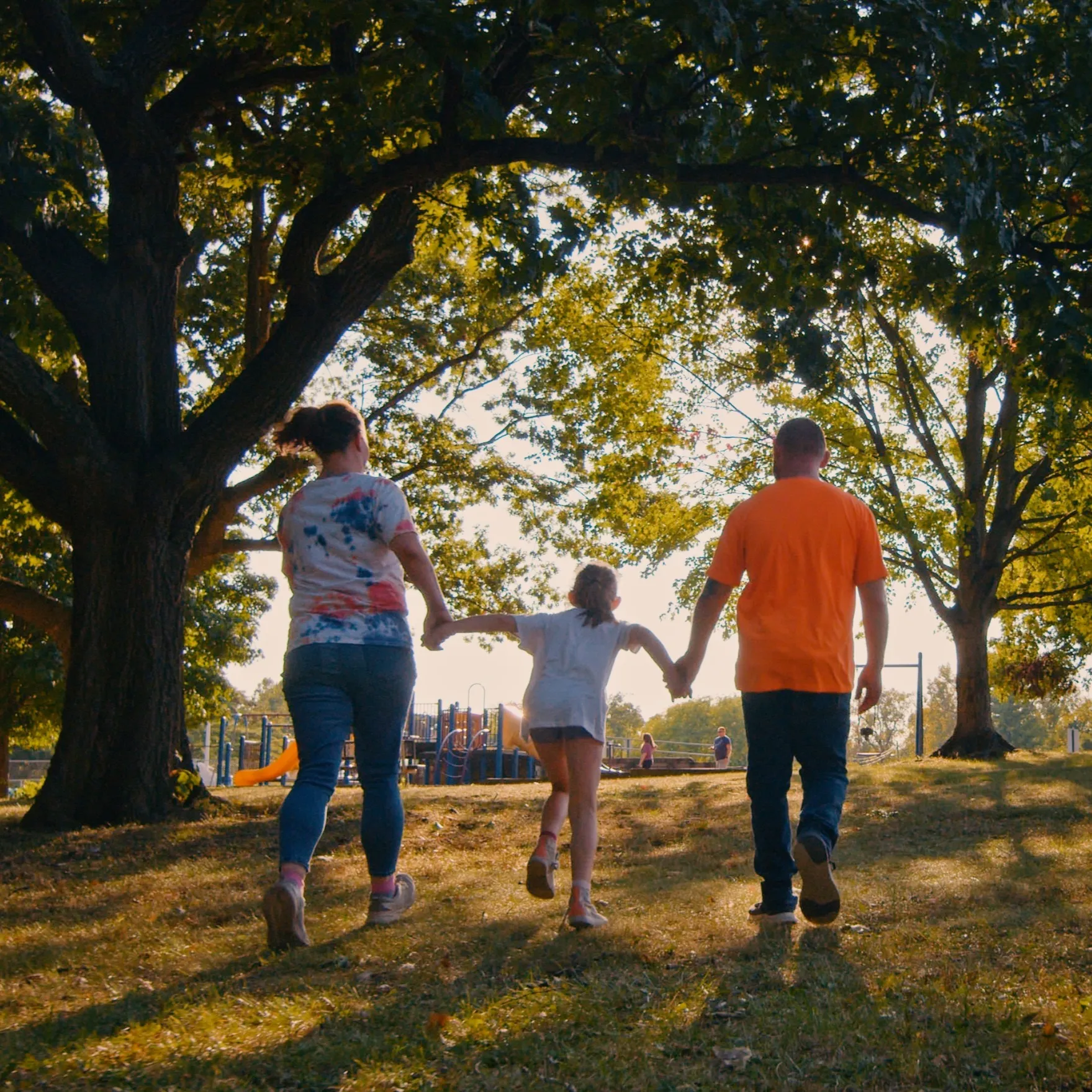 maddie and her parents hold hands and run toward the playground