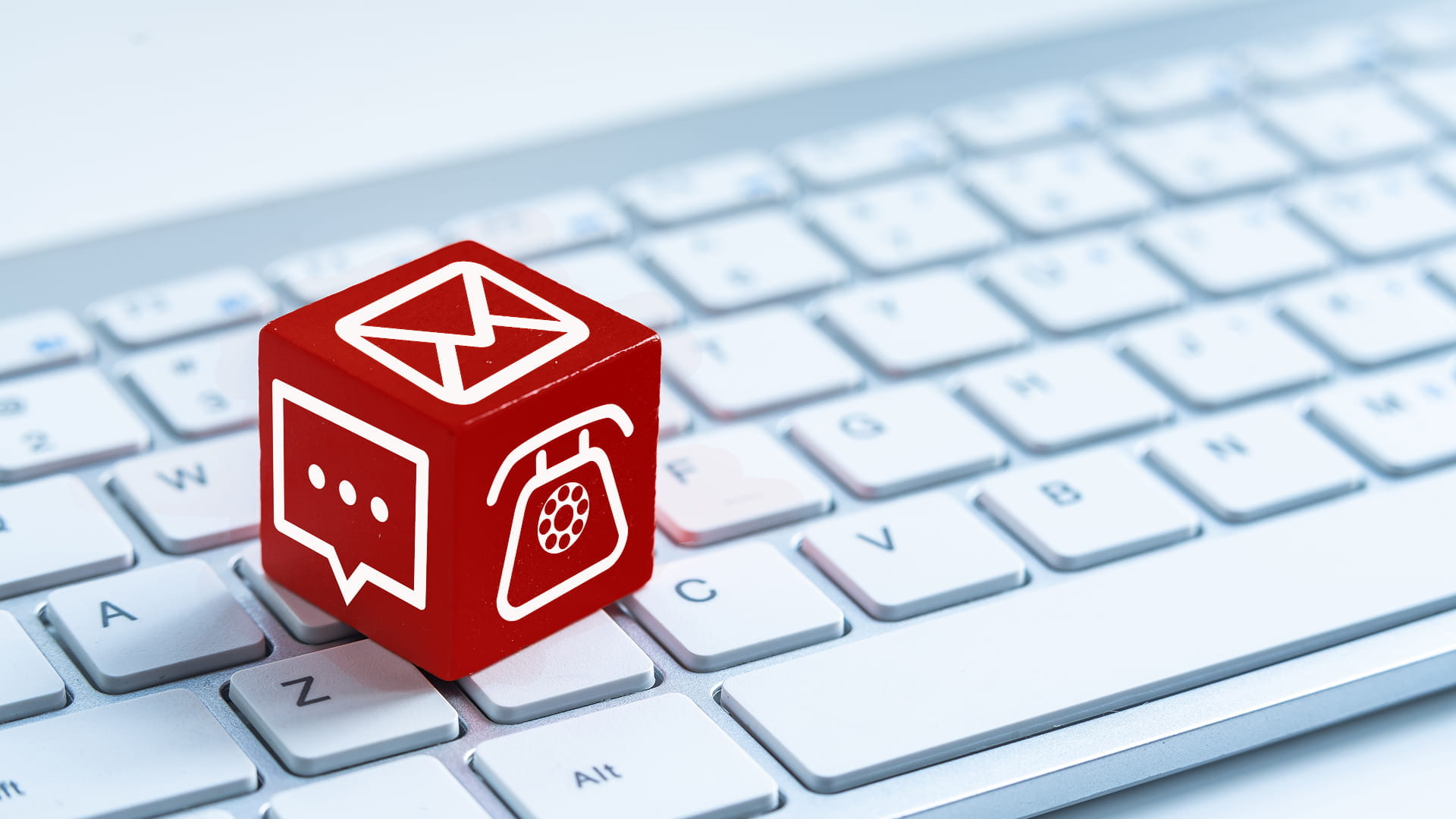 Red cube with icons for email, messaging, and phone placed on a computer keyboard.