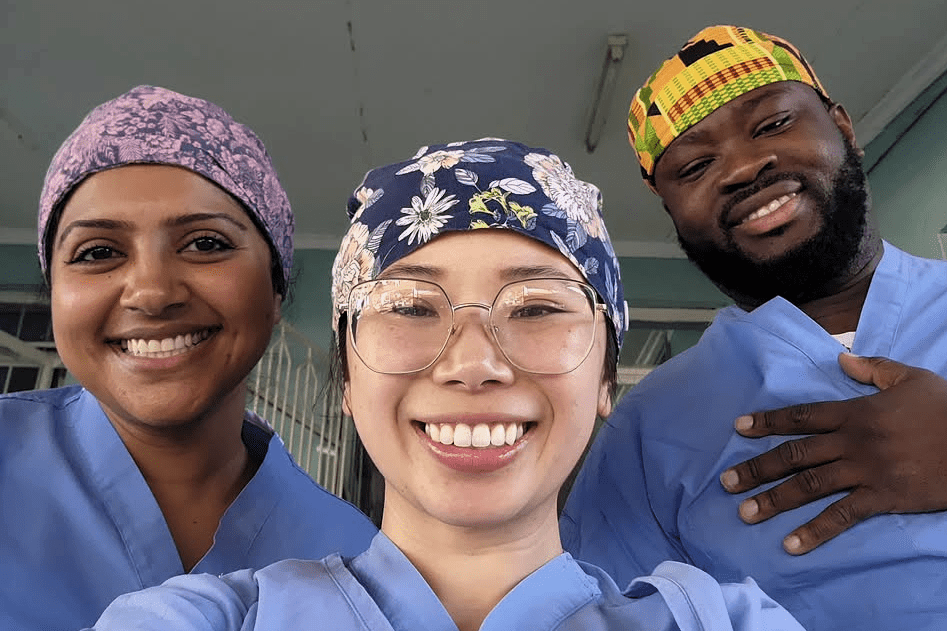 Three clinicians in blue scrubs and surgical caps pose close together for a photo in a clinical hallway.