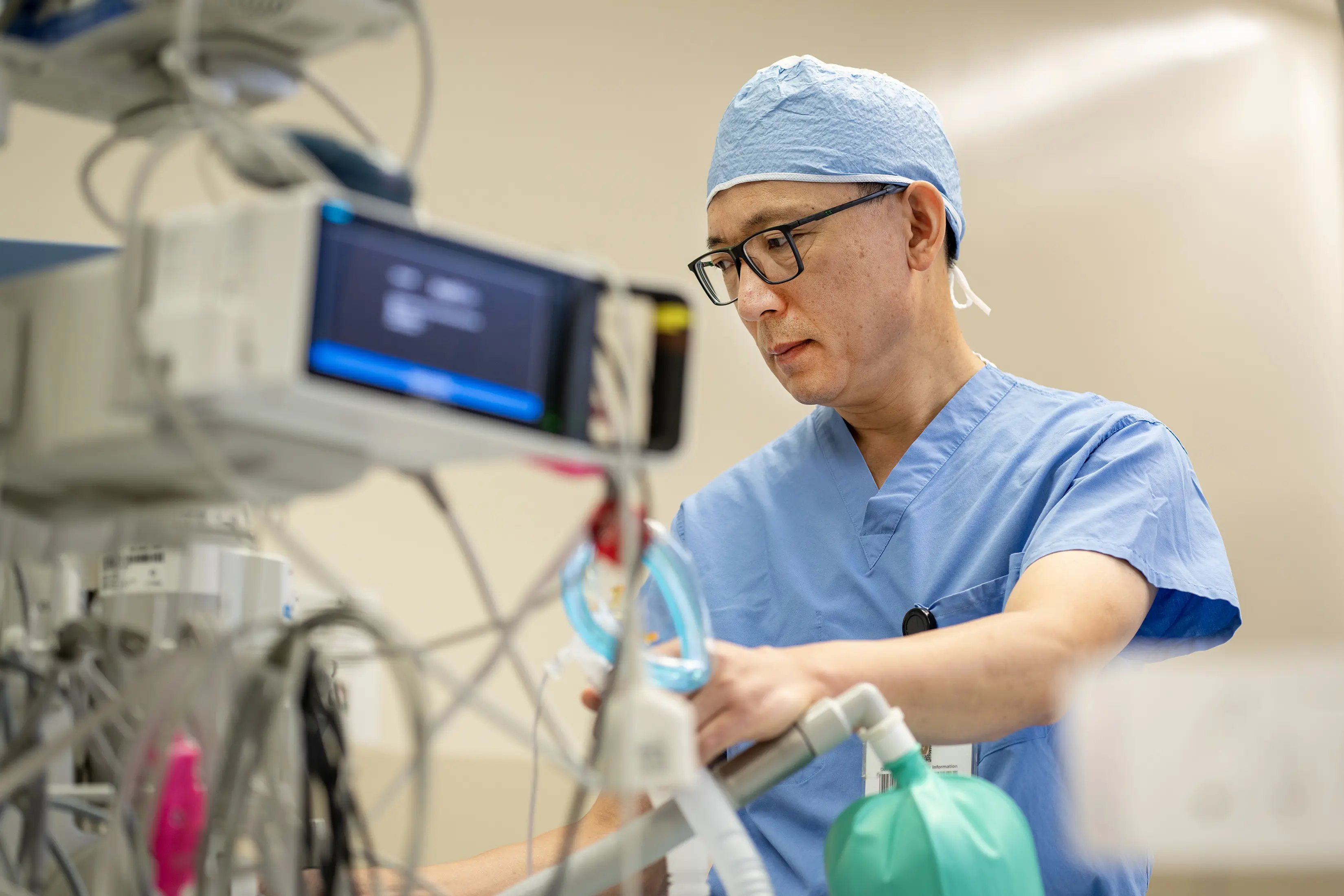 Clinician in surgical scrubs adjusts medical equipment in a hospital operating room.