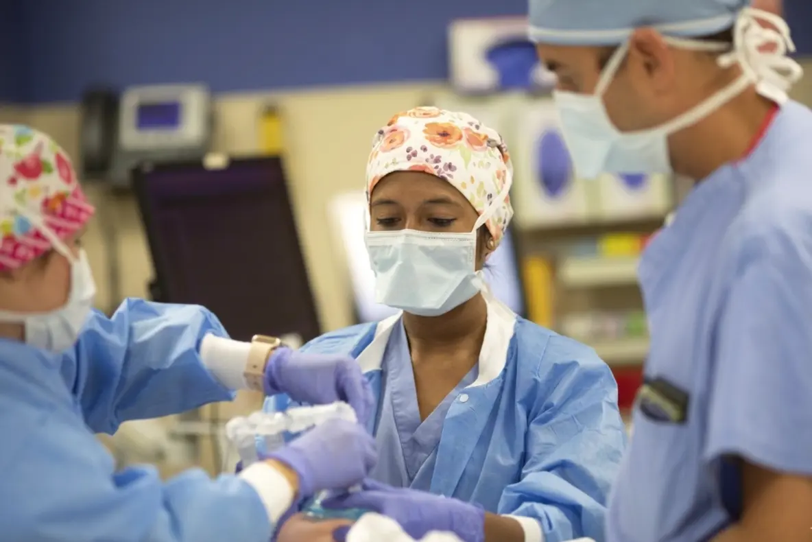 Medical team in surgical attire placing an airway mask on a patient in an operating room.