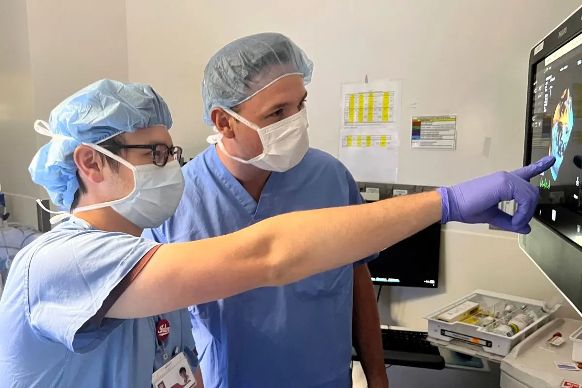 two physicians in surgical wear review information on a monitor in the operating room