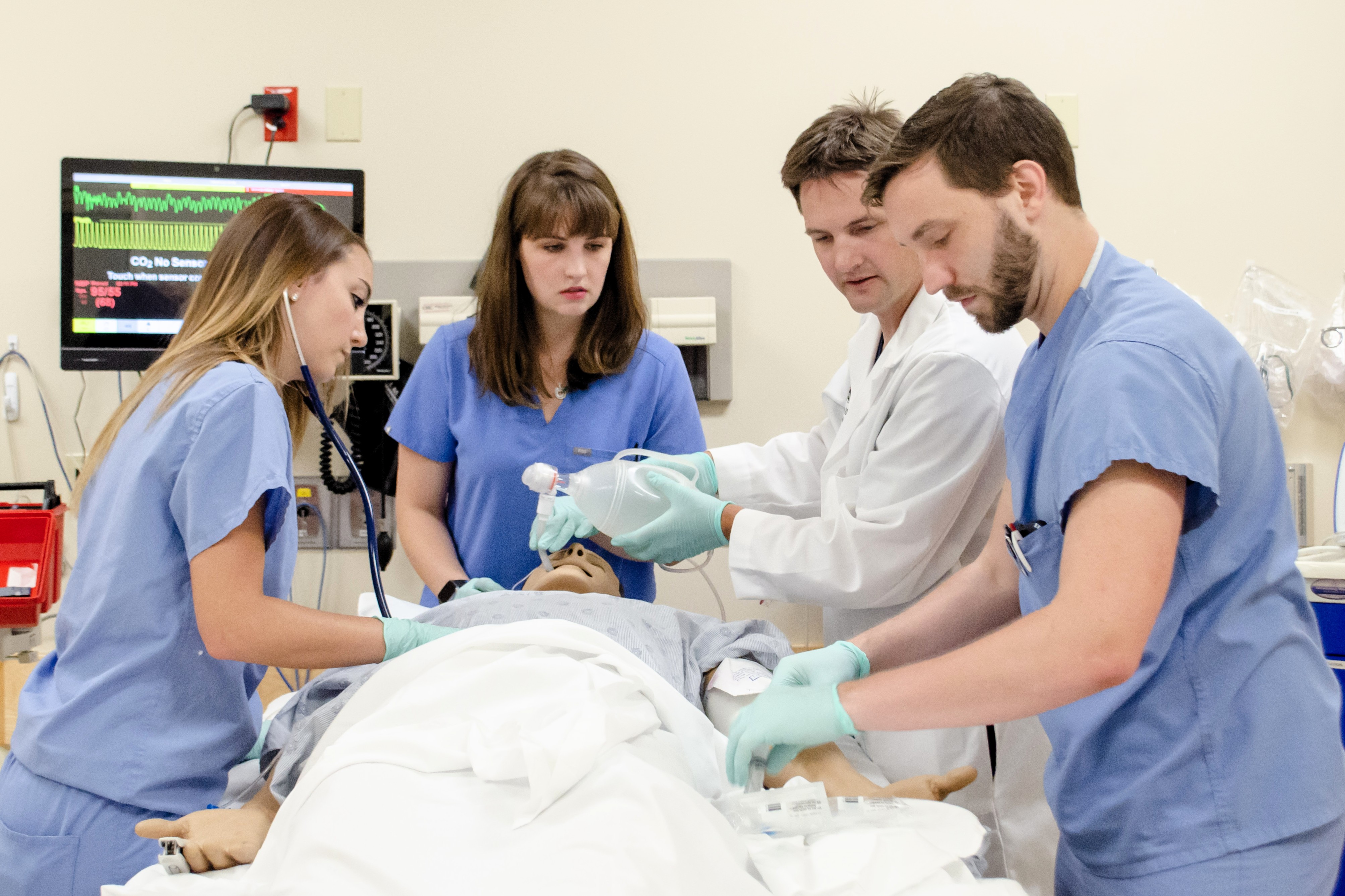 Medical team performs airway management on a simulation patient while monitoring equipment displays vital signs.