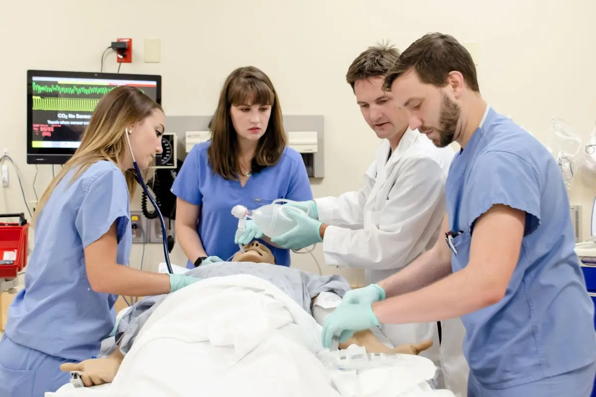 Medical team performs airway management on a simulation patient while monitoring equipment displays vital signs.