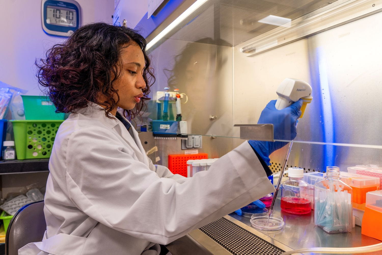 A researcher prepares a sample under the hood in the lab. She is wearing a lab coat and gloves.