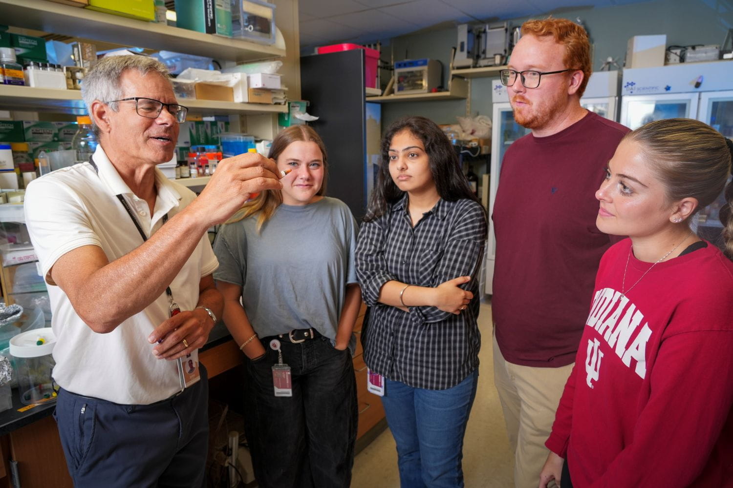 John Turchi and four members of his lab look at a sample together. Behind them are shelves of lab equipment and refrigeration units.