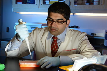 A researcher in a lab coat and gloves prepares lab samples with a pipette.