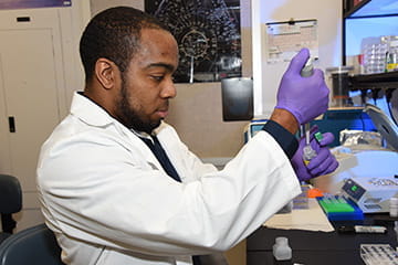 A man in a lab coat and gloves prepares a sample in the lab