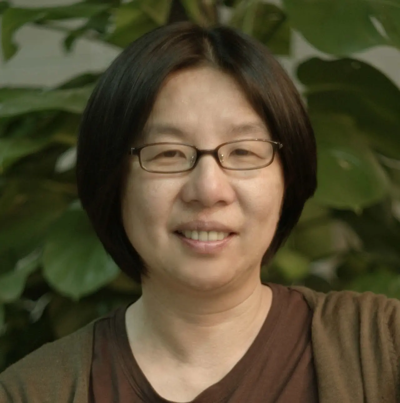 portrait of bin yu, an asian woman wearing glass in front of a leafy plant