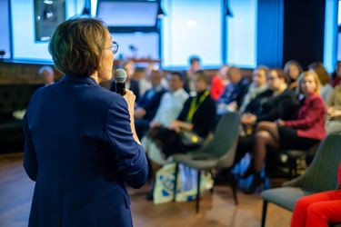 A woman in a suit speaks in front of an audience