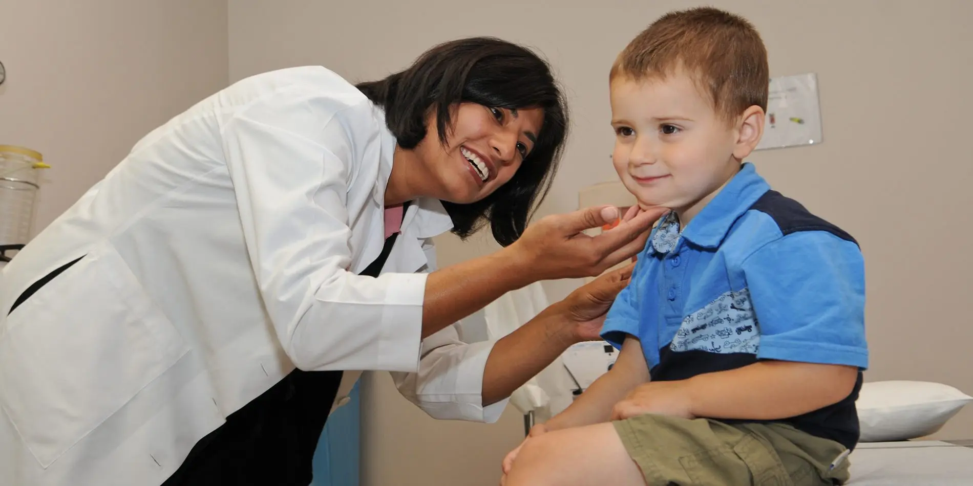 A small boy smiles while being examined by a doctor in a white coat
