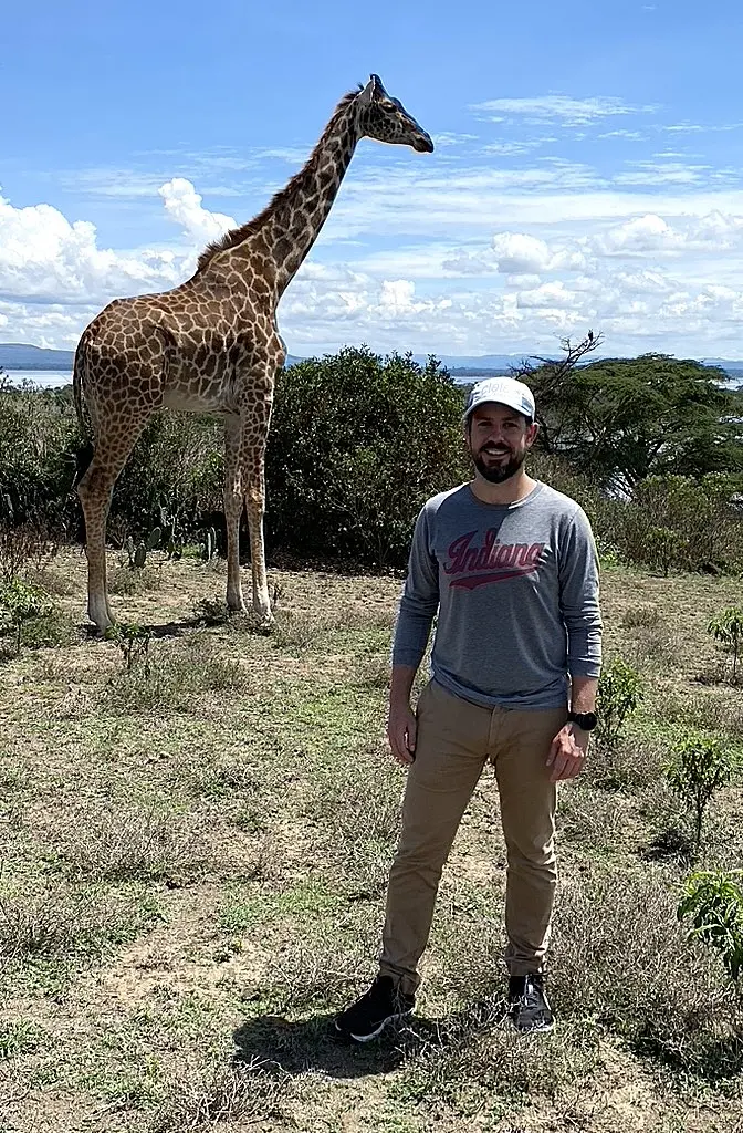 A faculty member stands next to a giraffe. 
