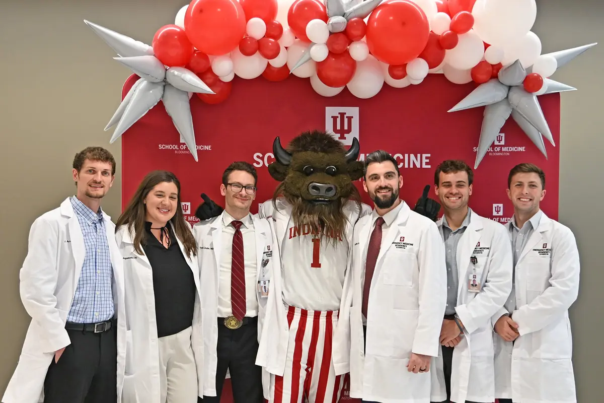 six residents in white coats stand with IU's mascot Hoosier the buffalo