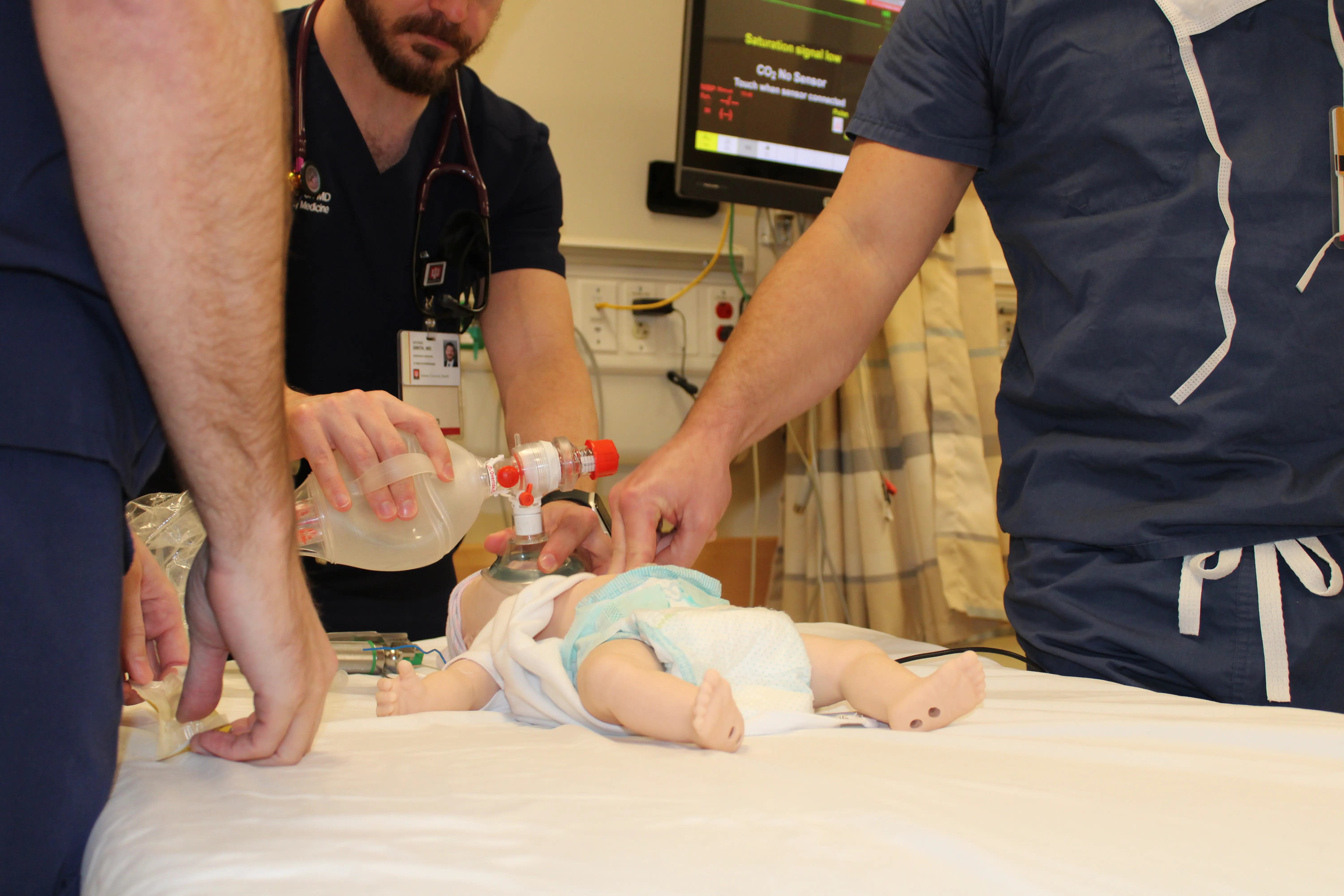 Physicians providing air to an infant patient mannequin. 