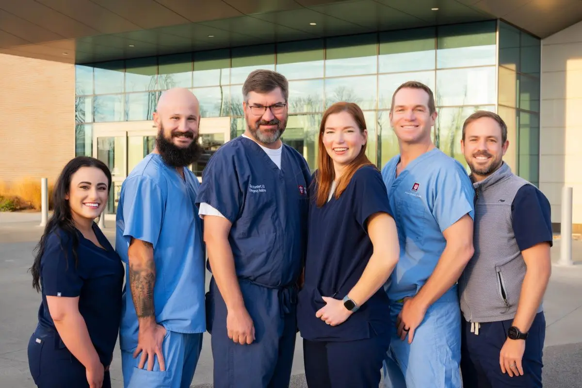 A group of physicians smiles in front of the IU Health Bloomington hospital. 