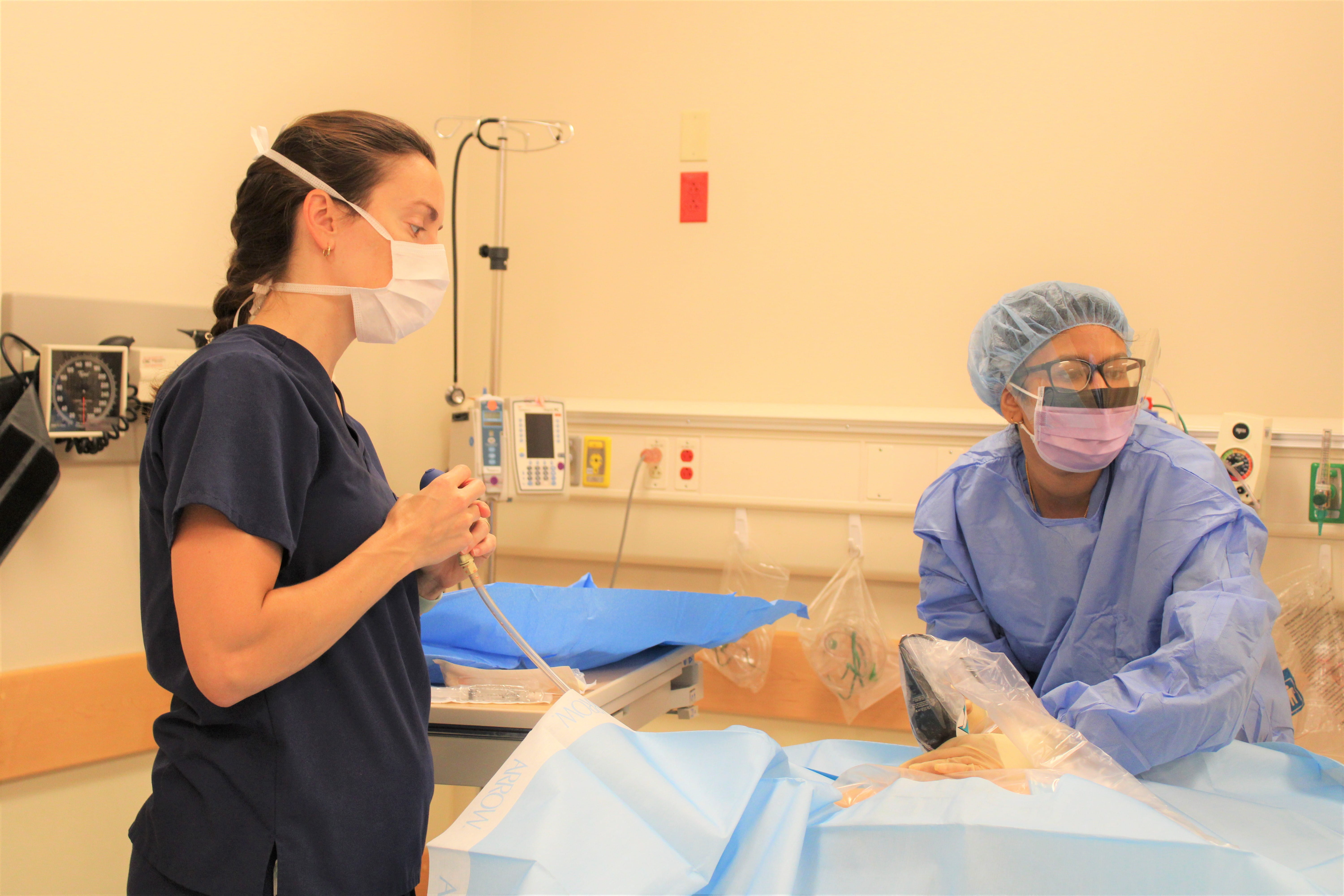 a fellow and faculty member review trainees in the ambulance simulation bay