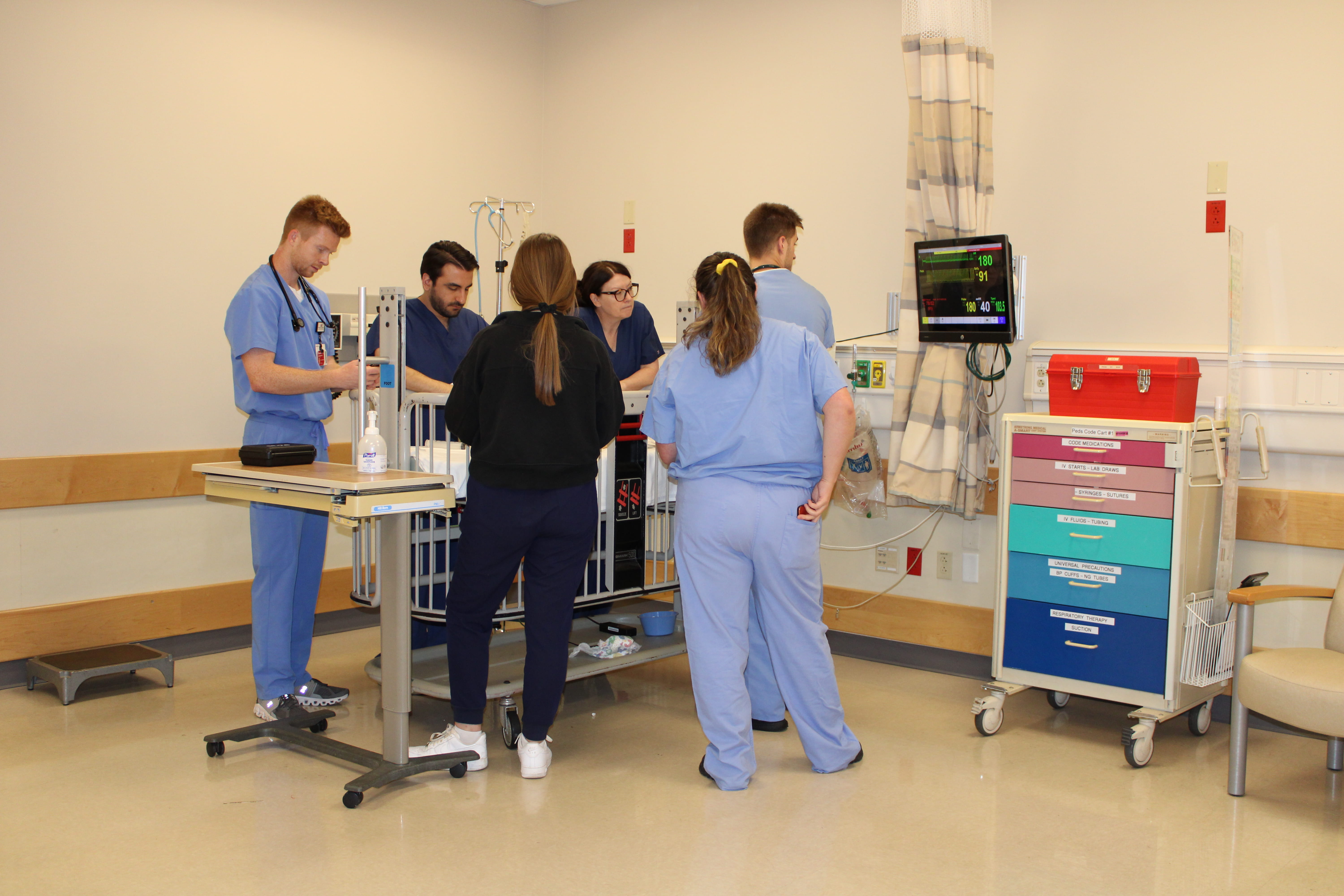 Medical students surround a baby mannequin patient during a pediatric emergency medicine simulation case.