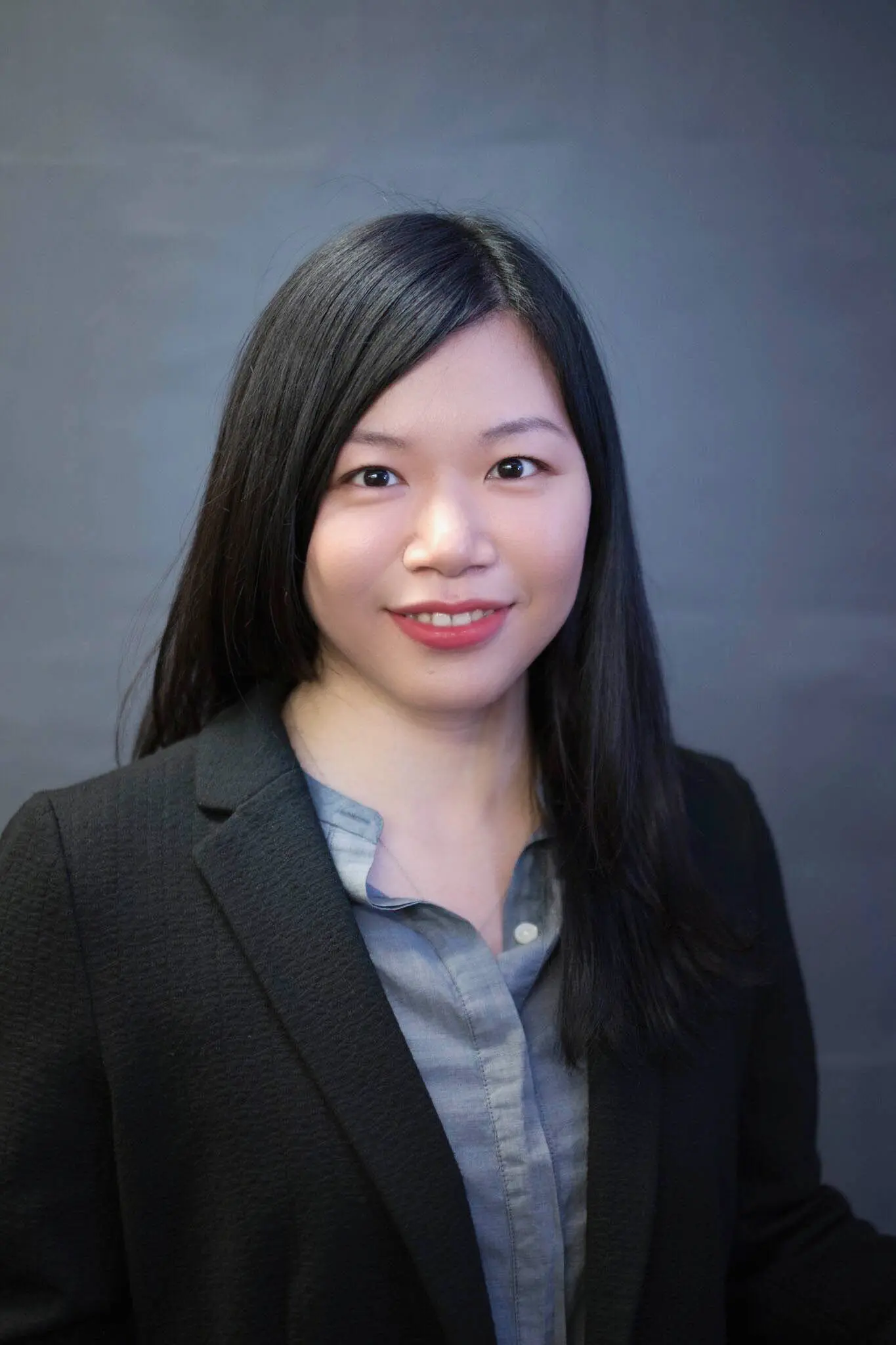 esther chang wearing a black jacked over a grey shirt. she has long straight black hair.