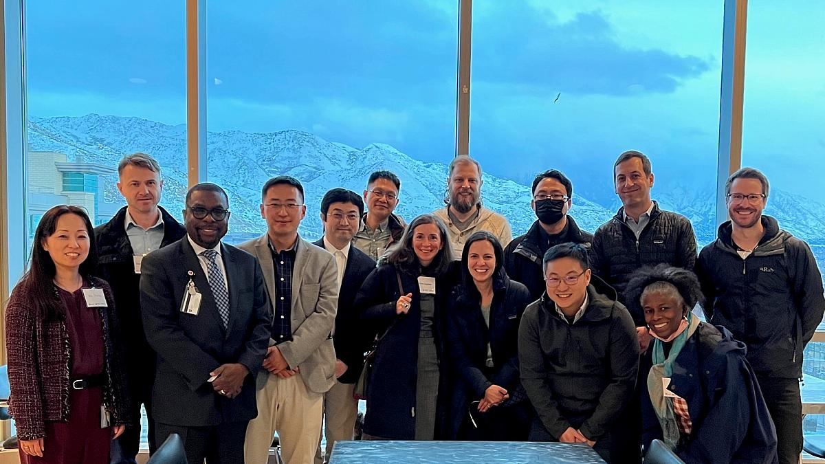 members of the course stand in front of a large window overlooking snowy mountains in salt lake city