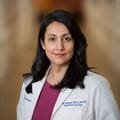 Gita Suneja has long dark hair and wears a white lab coat