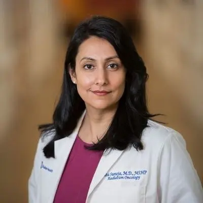 Gita Suneja has long dark hair and wears a white lab coat