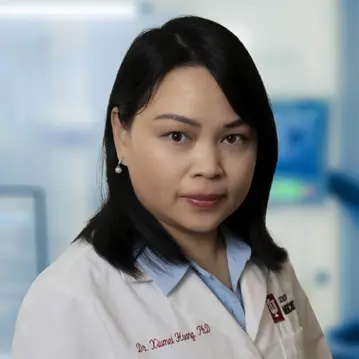 Xiumei Huang wearing a white lab coat standing in her lab space
