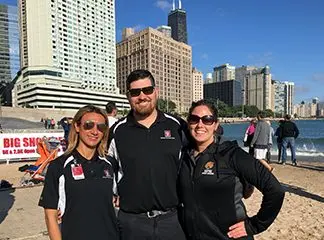 Three physicians stand together in front of a city beach