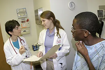 Two physicians and a patient speak together in an exam room