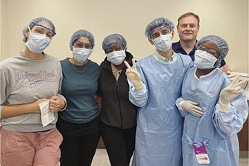 six residents in masks and scrubs stand with their arms around each other