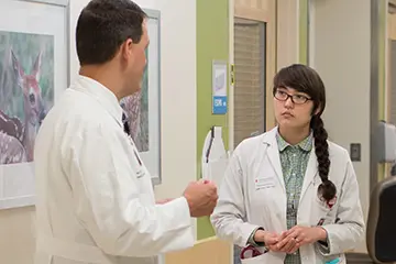 A resident listens to a faculty member in the hospital hall way
