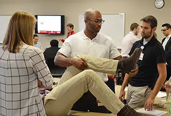 A physician holds a prone person's knee and lower leg while teaching medical students in class