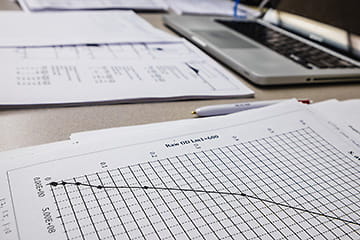 A paper with a graph on it lies in the foreground, with a computer in the background.