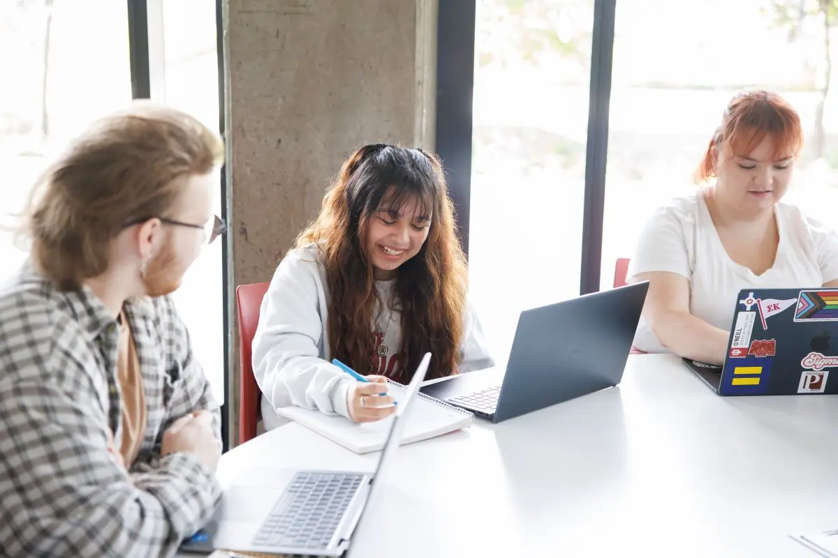 Students sit around a table with open laptops and discuss a journal article