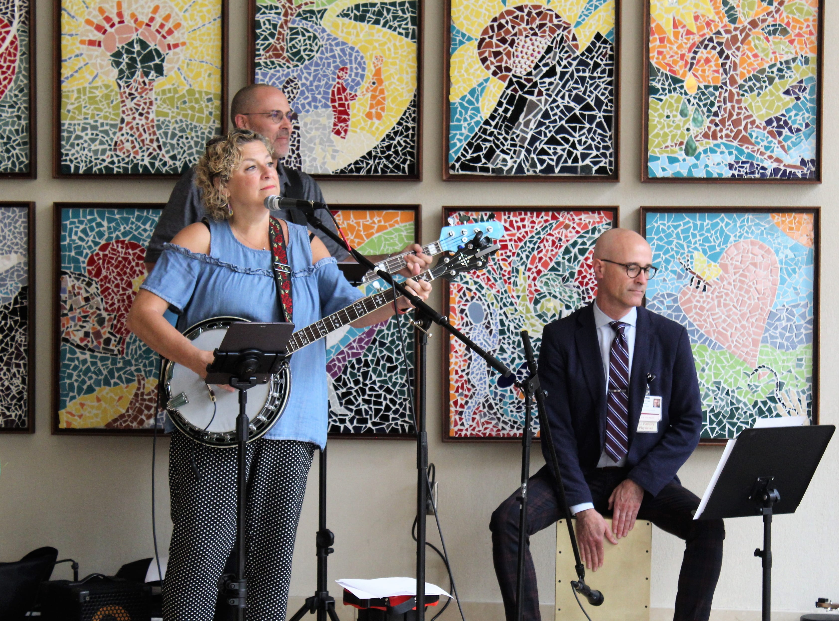 Department of Medicine Chair David Aronoff sits atop a wooden, box-like cajon drum in the lobby of the Simon Cancer Center as he plays with three other members of the band "the Crooked Finger Rhythm Review." The band includes a banjo player and two guitar players. Colorful artwork is displayed on the wall behind the band.