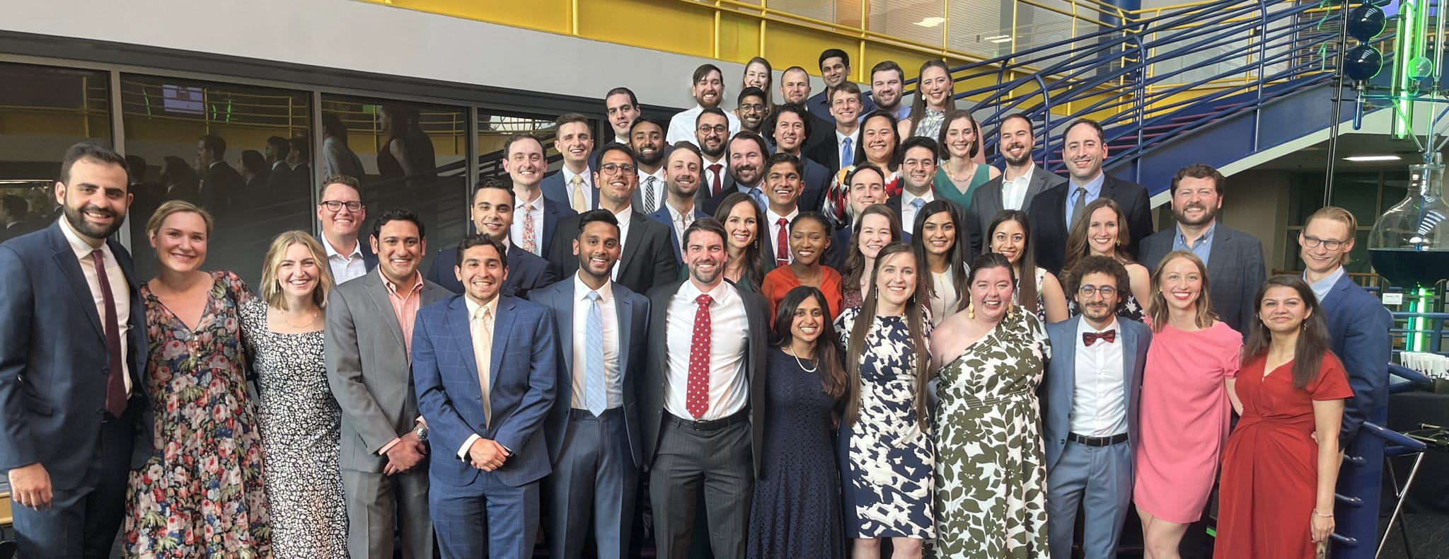 a large group of diverse internal medicine residents pose for a picture on a blue staircase at a graduation event at the Indianapolis children's museum