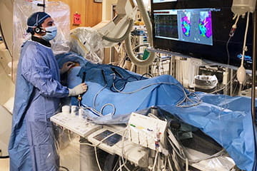 a fellow caring for a patient with a large monitor in the background