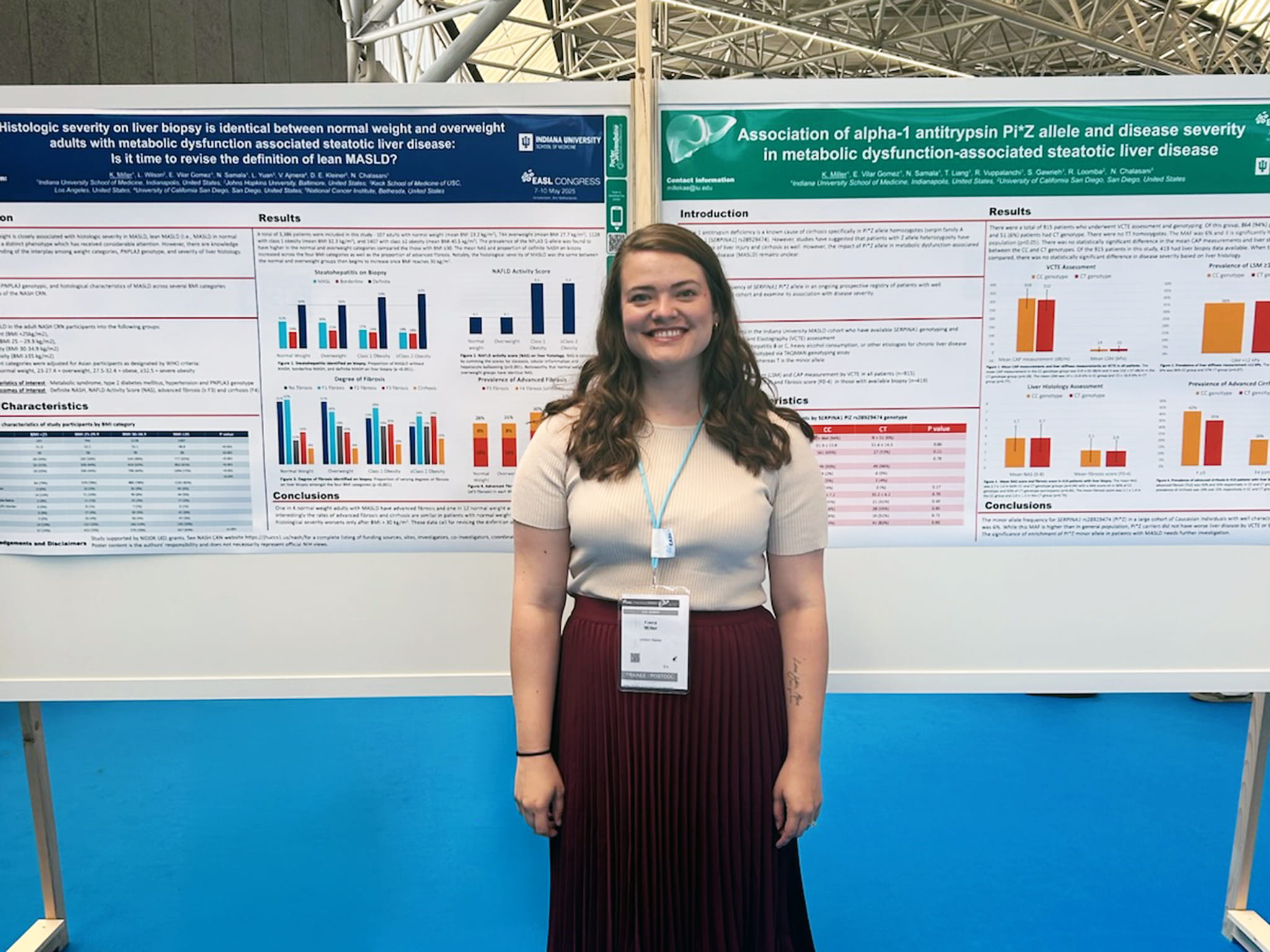 Kaela Miller at an exhibit hall smiling and standing in front of her EASL 2025 posters