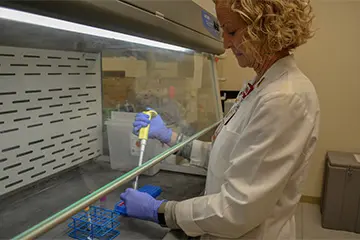 a researcher in a white coat prepares a sample under the hood in a lab