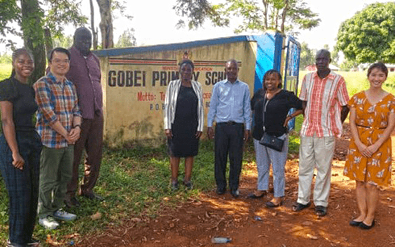 Tuan Tran (middle left) standing with colleagues in front of Gobei Primary School sign in Africa. | Photo courtesy Tuan Tran
