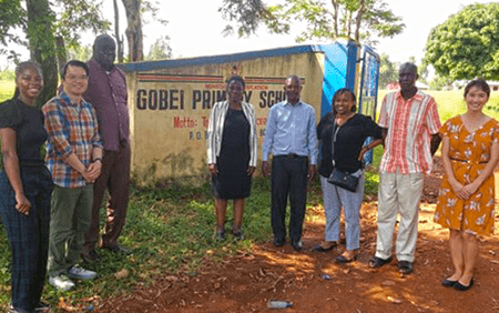 Dr. Tuan Tran (middle left) standing with colleagues in front of Gobei Primary School sign in Kenya. | Photo courtesy Tuan Tran Tuan Tran (middle left) standing with colleagues in front of Gobei Primary School sign in Africa. | Photo courtesy Tuan Tran