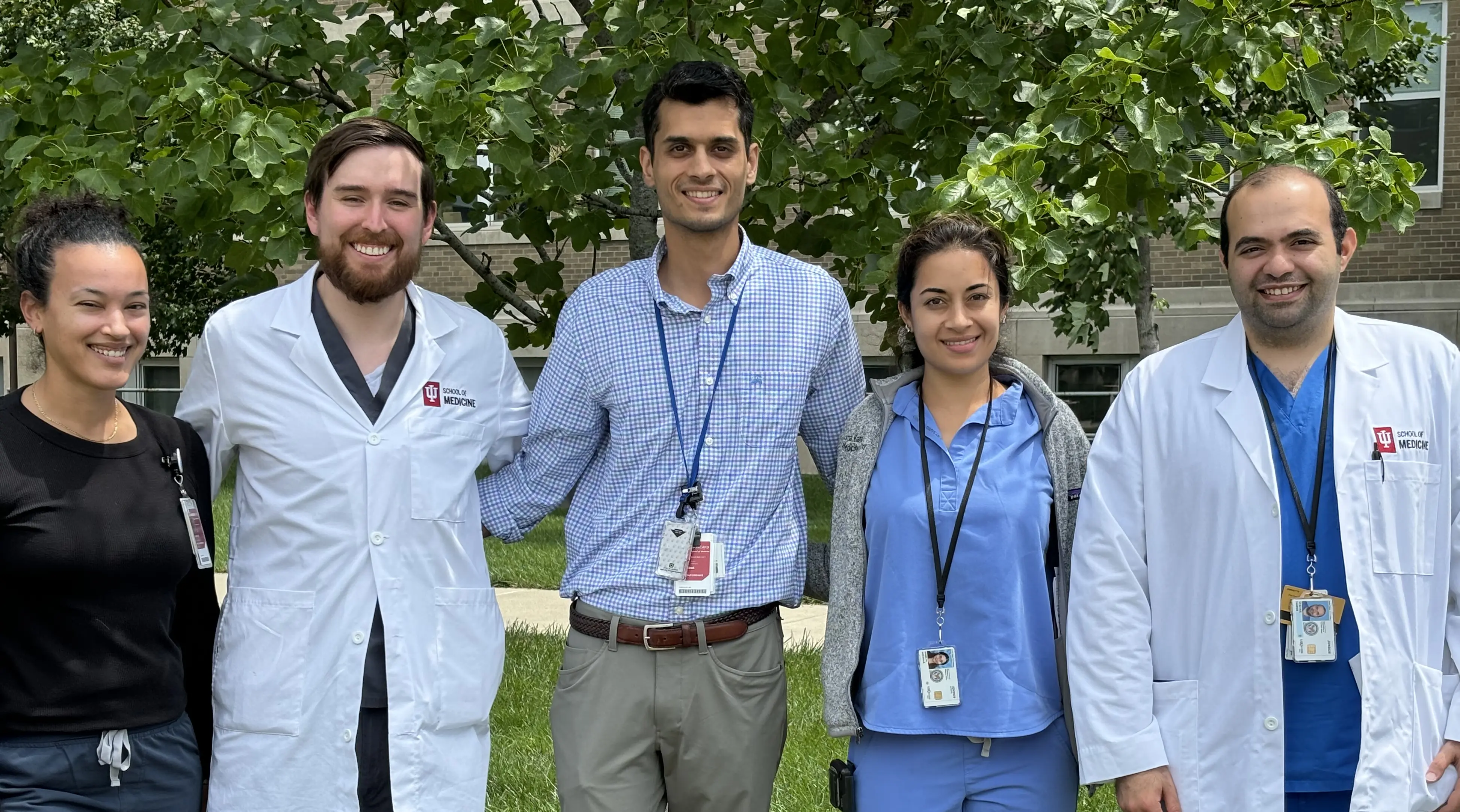 five physicians stand together smiling outside on a sunny day