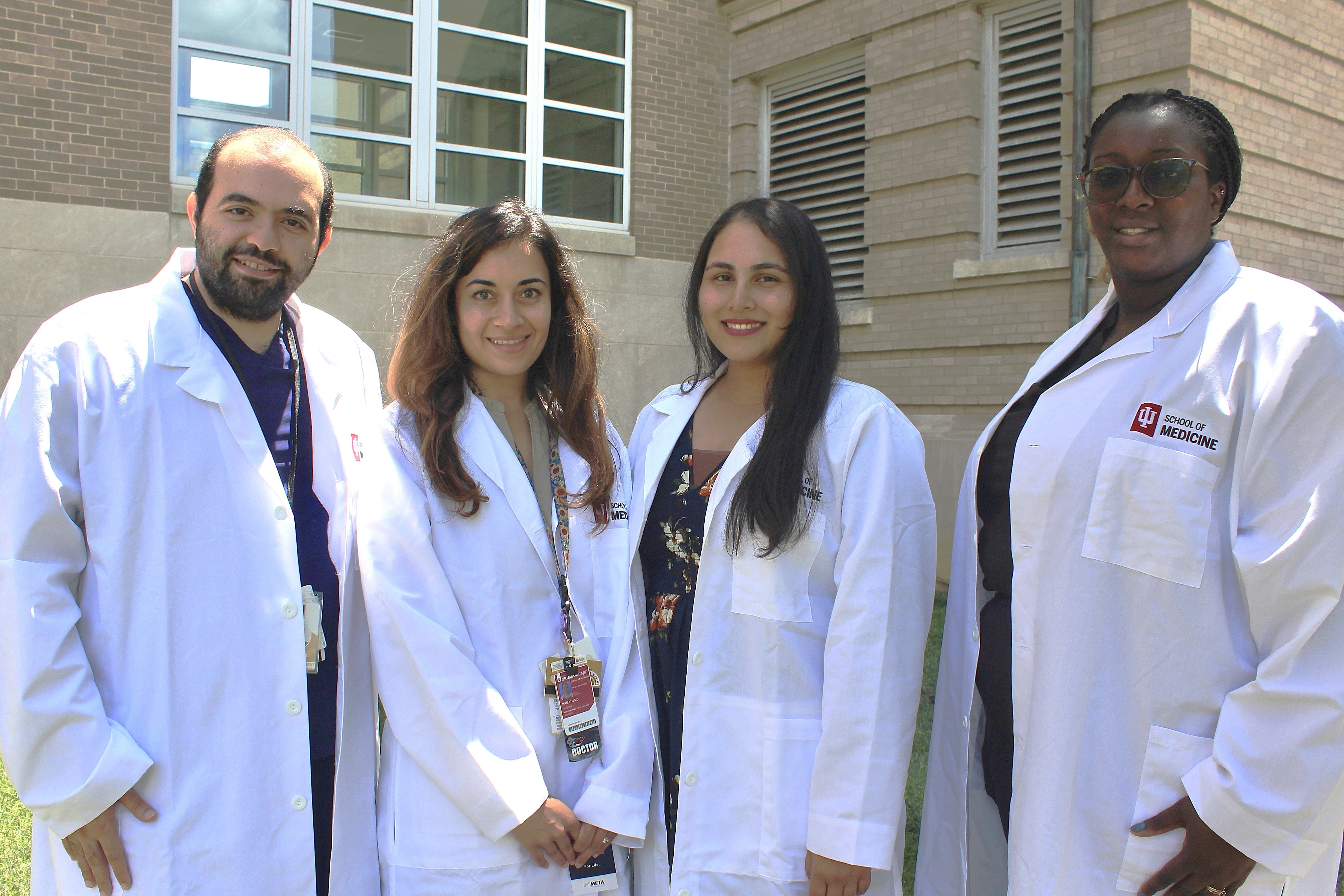 Hamed Chehab, Aneesha Kamath, Keeret Mann, and Theresa Emeli stand outside in white coats
