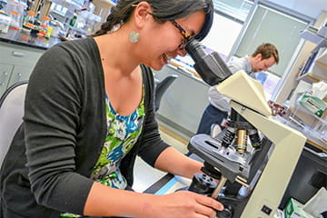 a woman examines a sample through a microscope