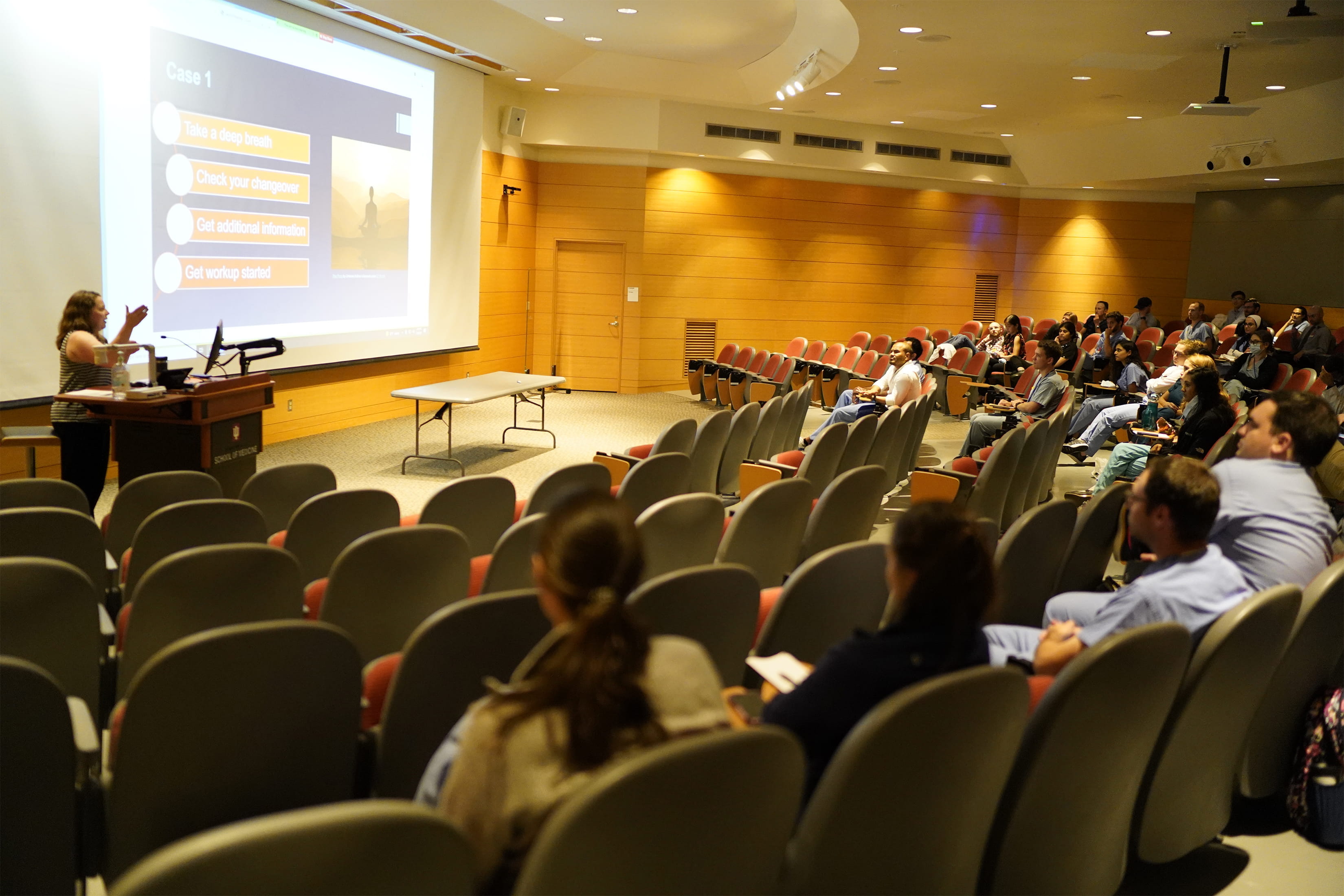 Trainees sit and listen to a lecture in a large lecture hall.