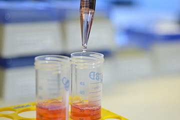 a close up image of a pipette adding solution to a lab sample