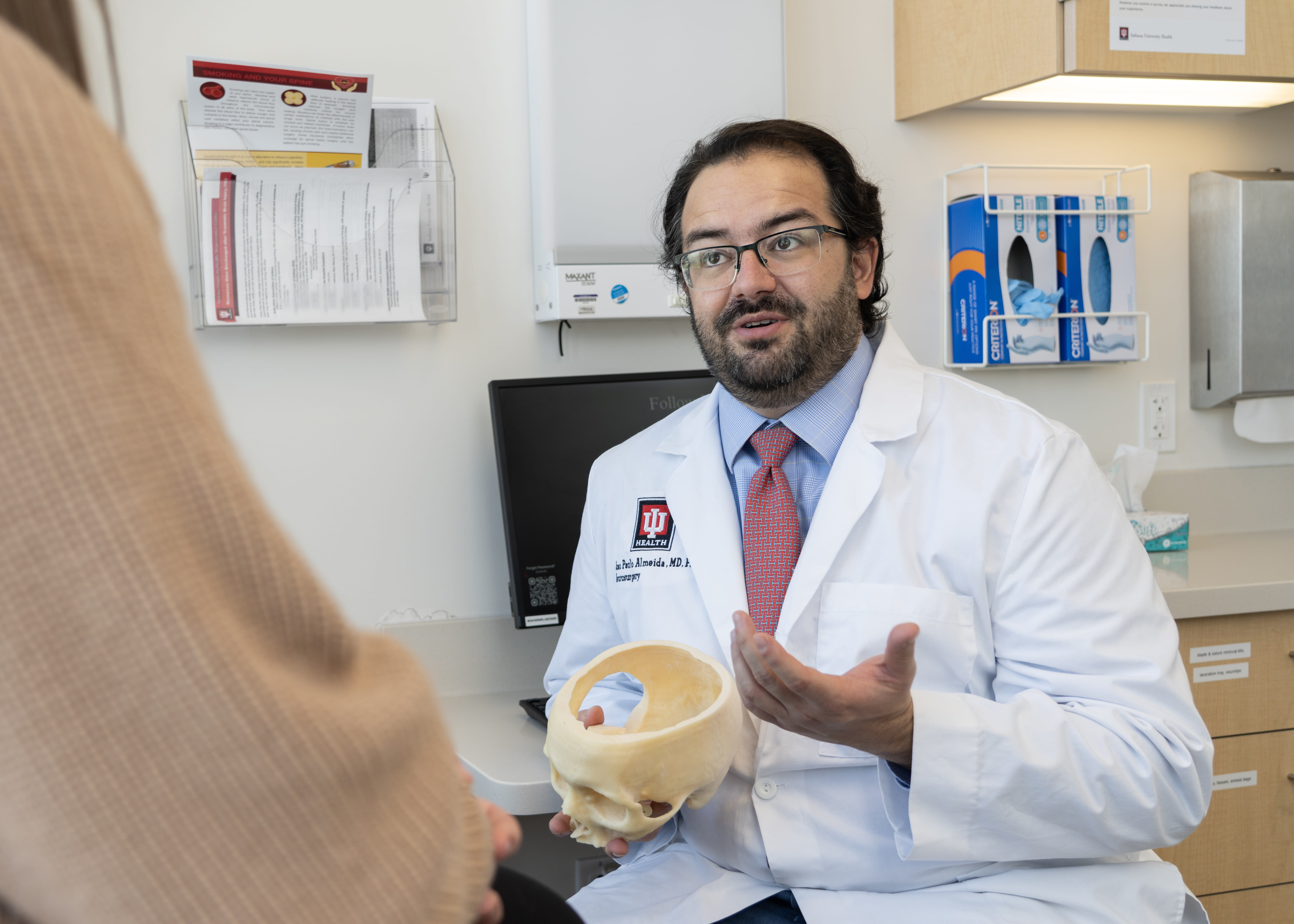 A neurosurgeon uses a skull model to demonstrate to a patient in clinic 