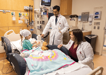 Two physicians in a hospital room speaking with a small child in bed